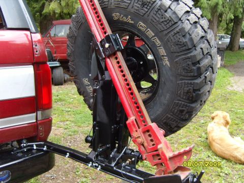 1989 Ford Bronco - Rear view of a red SUV with a spare tire and Hi-Lift jack attached to the bumper.
