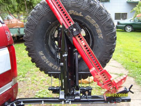 1989 Ford Bronco - Spare tire carrier with a Hi-Lift jack attached to the rear of a red vehicle.