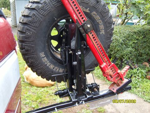 1989 Ford Bronco - A hi-lift jack is mounted to the spare tire carrier of a vehicle, with a dog resting in the background.