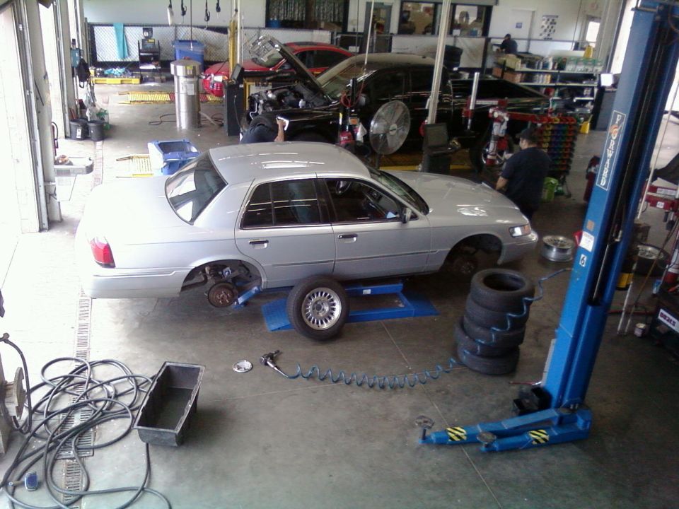 2000 Mercury Grand Marquis on lift with wheels removed, another car with hood open in background