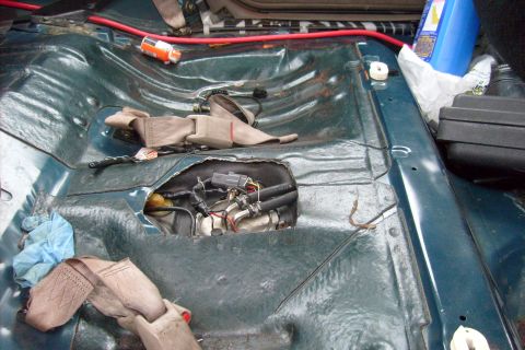1994 Mazda 626 - The interior floor of a car is exposed, revealing the fuel pump assembly and wiring beneath the carpet.