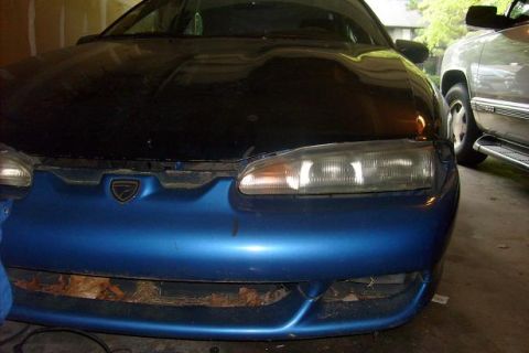 1994 Mazda 626 - Front view of a car with a blue bumper and black hood, parked next to a silver SUV.