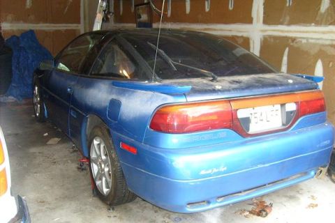 1994 Mazda 626 - Blue coupe with a spoiler and custom bumper text sits in a garage.