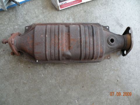 1994 Acura Integra - A catalytic converter sits on a concrete surface, showing signs of rust and wear.