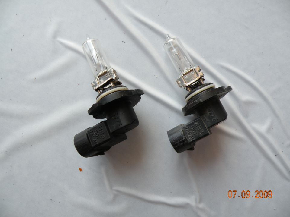 Two clear glass automotive headlight bulbs with black plastic bases on a white cloth