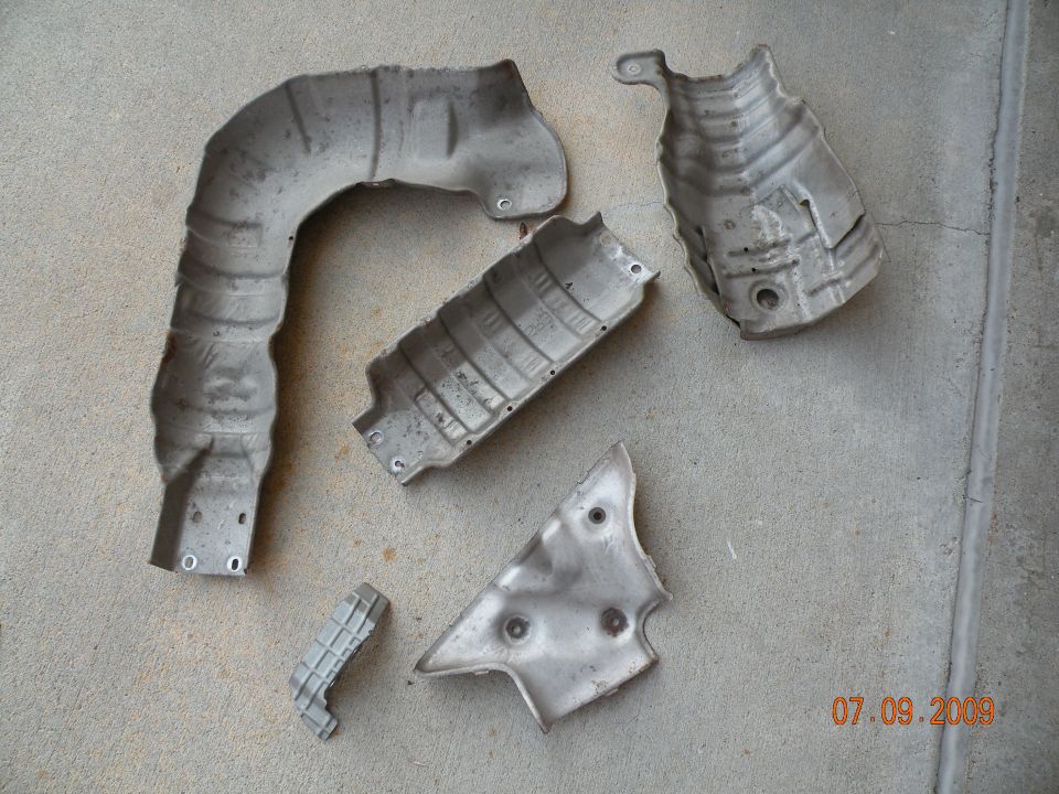 Several metal heat shields laid out on concrete