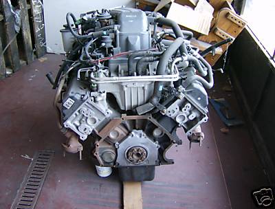 1993 Ford Crown Victoria - A complete V8 engine assembly sitting on a wooden pallet, viewed from the front showing the timing cover, crankshaft pulley area, intake ma…