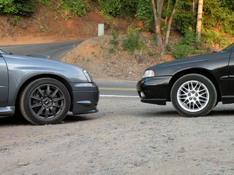1998 Subaru Legacy - A grey Subaru and a black Subaru are parked side-by-side on a gravel shoulder.