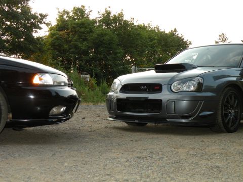 1998 Subaru Legacy - Two Subaru Impreza WRX STIs are parked side-by-side on a gravel lot, with the grey car a prominent hood scoop.