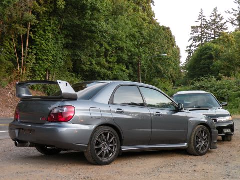 1998 Subaru Legacy - A gray Subaru WRX STI sedan is parked on a dirt road, with another Subaru visible behind it.