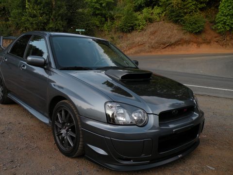 1998 Subaru Legacy - This Subaru Impreza WRX STI is parked on a dirt road next to a paved road with trees in the background.