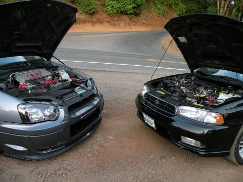 1998 Subaru Legacy - A grey Subaru WRX STI and a black Subaru Legacy are parked side-by-side on a dirt road, both with their hoods open.