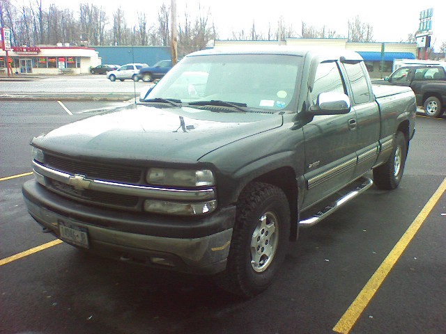 Dark green pickup truck, front quarter view, chrome side steps, aftermarket wheels, parked in a lot