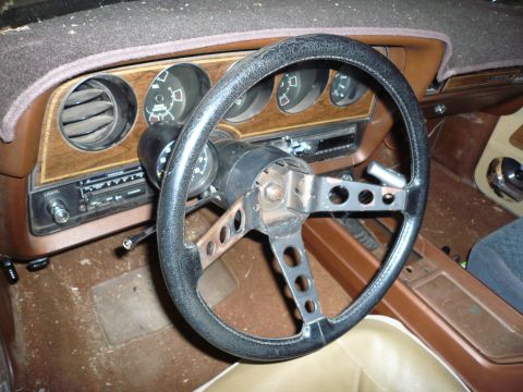 1975 Ford Ranchero - The interior of a 1975 Ford Ranchero features a worn steering wheel and a wood-grain dashboard with a radio.