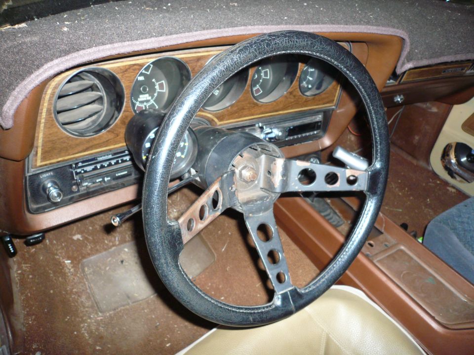 1975 Ford Ranchero interior showing cracked steering wheel, wood-grain dash, and radio