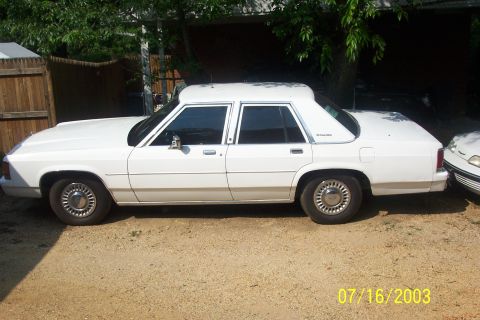 1991 Ford LTD Crown Victoria - White Ford LTD Crown Victoria four-door sedan in driver's-side profile on a gravel drive, with an LTD Crown Victoria script badge on the re…