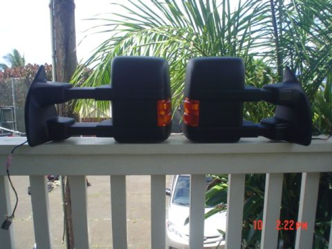 2005 Ford Excursion - Two black tow mirrors with amber turn signals are displayed on a white railing, with a white car partially visible behind them.