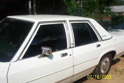 1991 Ford LTD Crown Victoria - Passenger-side view of a white Ford LTD Crown Victoria four-door sedan with tinted windows, chrome window trim and a large chrome-housed si…