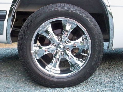 2002 Chevrolet Silverado 1500 - A close-up of a chrome wheel and tire on a white vehicle, showing custom aftermarket rims.