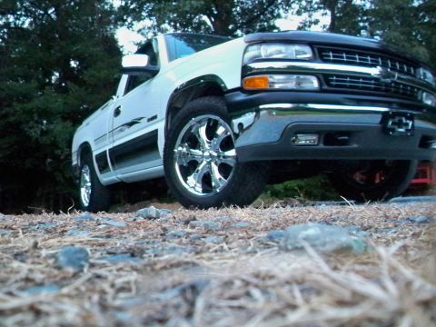 2002 Chevrolet Silverado 1500 - A white 2002 Chevrolet Silverado 1500 pickup truck is viewed from a low angle, highlighting its chrome wheels and front grille.