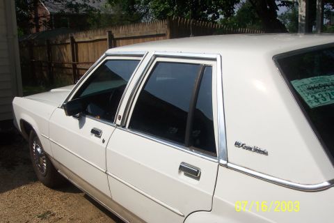 1991 Ford LTD Crown Victoria - Close-up of the driver's side of a white Ford LTD Crown Victoria sedan, showing the chrome window surrounds, tinted glass, chrome door hand…