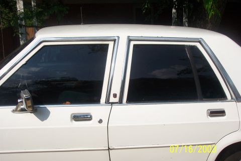 1991 Ford LTD Crown Victoria - Close-up of the driver's side of a white four-door sedan, framed on the front and rear door glass with heavy dark window tint and bright ch…