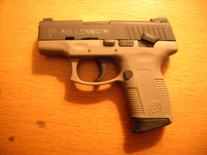 Tan Millennium pistol with black grip extension on a wooden surface