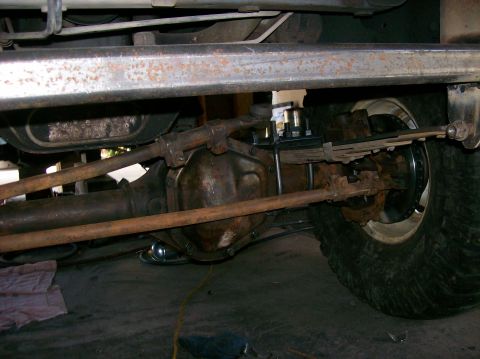 1989 Ford Bronco - Close-up view of the front axle and suspension components of a vehicle, showing the steering mechanism and leaf springs.