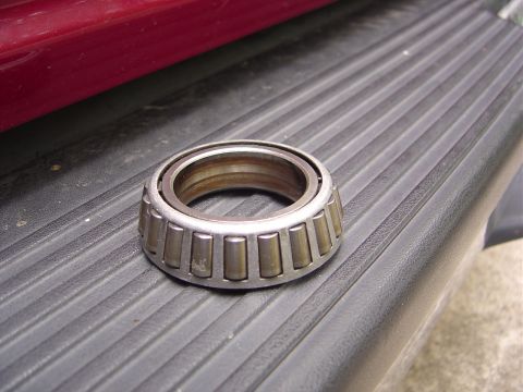 1986 Ford Bronco - A tapered roller bearing rests on a textured surface, with a portion of a red vehicle body visible in the background.