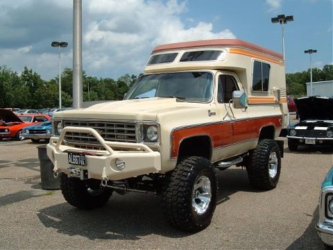 1991 Ford Bronco - Front three-quarter view of a lifted 1970s Chevrolet K5 Blazer Chalet-style camper conversion in tan with orange and brown stripes, parked…