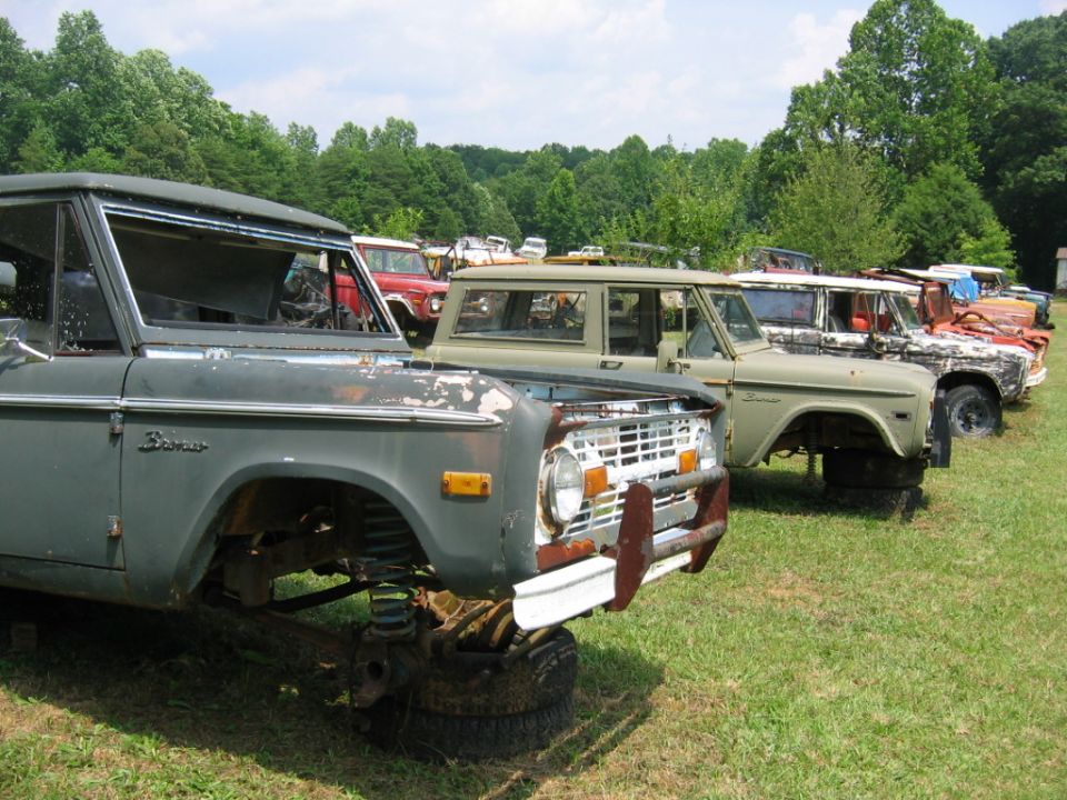 Row of derelict early Ford Broncos in a grassy field, front fenders removed