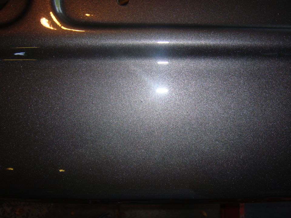 Close-up of metallic grey paint with reflections on a vehicle body panel