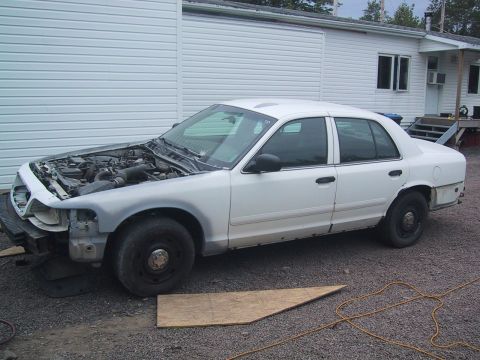 2003 Ford Crown Victoria - A white 2003 Ford Crown Victoria is parked outside with its hood up, revealing the engine compartment.