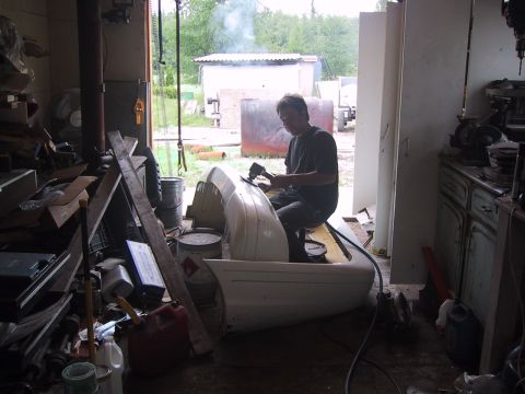 2003 Ford Crown Victoria - A man is seen working on a white car bumper inside a cluttered garage.