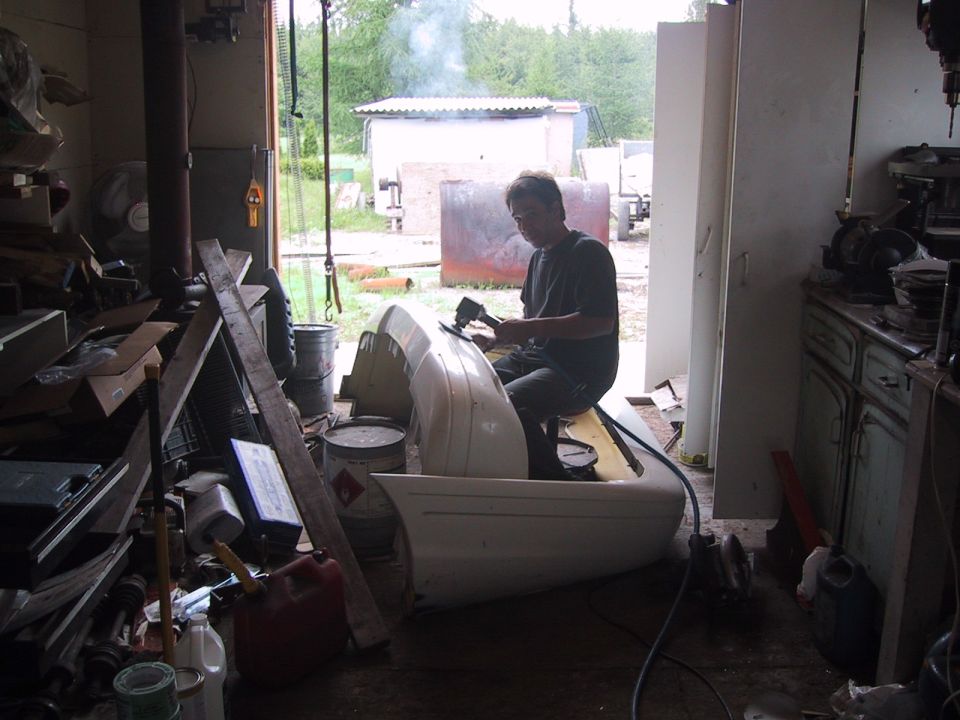 White car bumper being worked on by a man in a garage