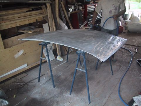 2003 Ford Crown Victoria - A person is sanding a car hood that is supported by sawhorses in a workshop.