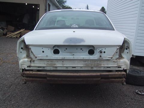 2003 Ford Crown Victoria - Rear view of a white 2003 Ford Crown Victoria with its bumper removed, revealing the underlying frame and structural components.