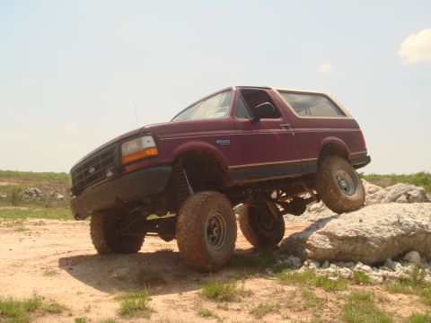 1992 Ford Bronco - A maroon 1992 Ford Bronco navigates a rocky terrain, demonstrating its off-road capabilities.