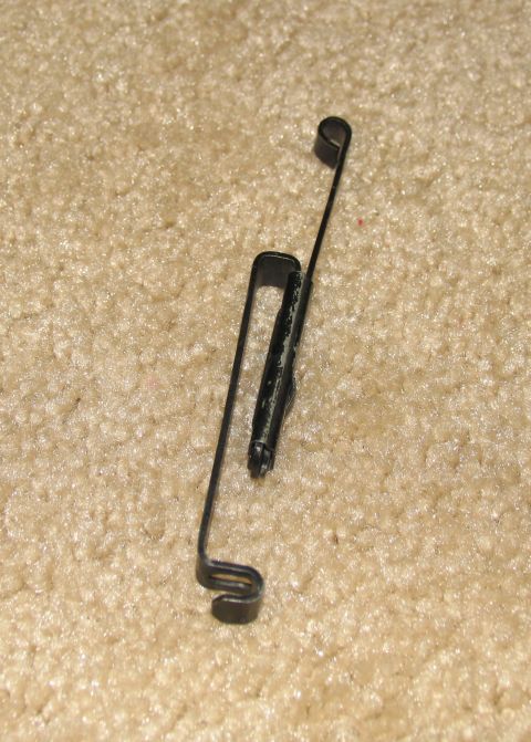 1984 Ford Bronco - A close-up view of a metal clip and spring assembly, likely a vehicle part, on a carpeted surface.