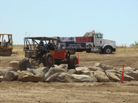 1989 Ford Bronco - An off-road buggy navigates a rocky obstacle course, with a tow truck and bulldozer nearby.