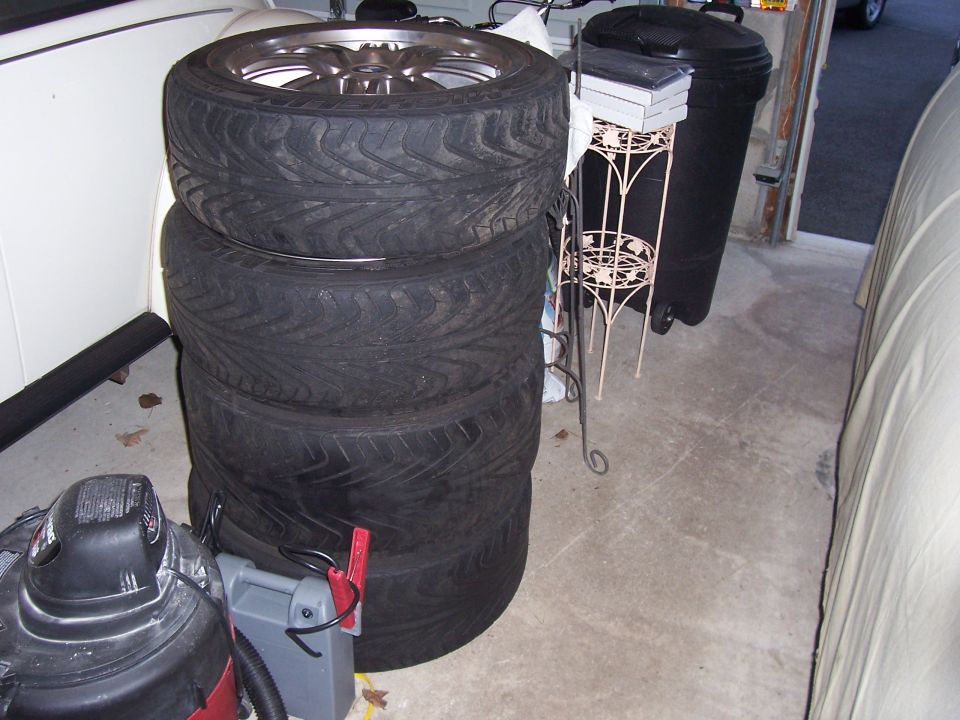 Stack of four tires on alloy wheels in a garage