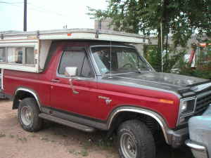 1991 Ford Bronco - This red Ford Bronco, equipped with a camper shell, is seen from a 3q-front angle. Its body style suggests an early 1980s model year.