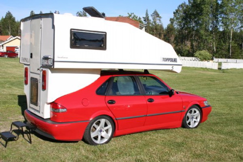 red Saab sedan with a white camper shell on top, parked on grass