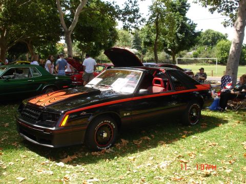 1978 Ford Mustang II - Outdoor car show features a black 1978 Ford Mustang II with distinctive orange graphics and red interior.