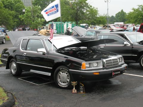 1985 Mercury Cougar - A black 1985 Mercury Cougar is displayed with its hood open, alongside trophies and other vehicles.