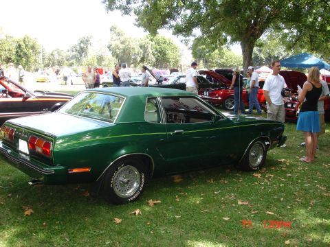 1978 Ford Mustang II - A green coupe with a vinyl roof is displayed at an outdoor car show, with other vehicles and attendees visible in the background.