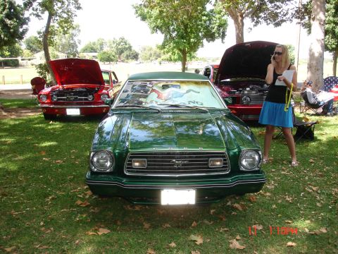 1978 Ford Mustang II - A green 1975 Ford Mustang II is parked on grass, with other cars and people in the background.