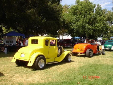 1978 Ford Mustang II - A yellow coupe hot rod is seen from the rear, towing an orange roadster at an outdoor car show.