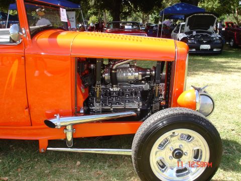 1978 Ford Mustang II - A close-up of a custom orange hot rod shows its powerful engine and chrome details at an outdoor car show.