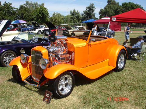 1978 Ford Mustang II - A bright orange hot rod convertible is displayed at a car show, a prominent chrome engine and custom wheels.